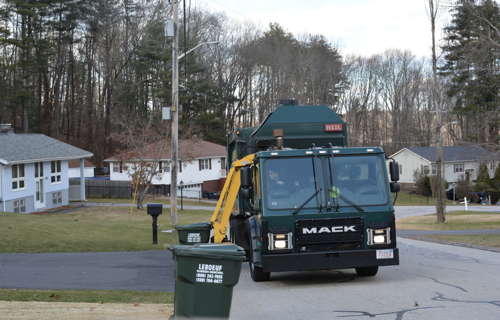 Garbage truck approaching a garbage bin in a residential neighborhood.